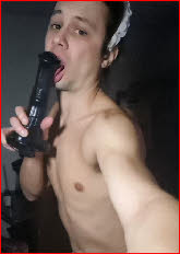 Exposed sissy Gabriel licking the tip of a big black dildo